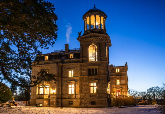 Schloss Kaarz mit Blick vom Mammutbaum zum hellbeleuchtetem Schloss in blauer Stunde mit Schnee