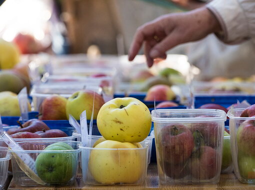 Verschiedene Äpfel in Plastikbehältern auf einem Marktstand, darunter gelbe, grüne und rote Sorten. Eine Hand greift nach einem Apfel.