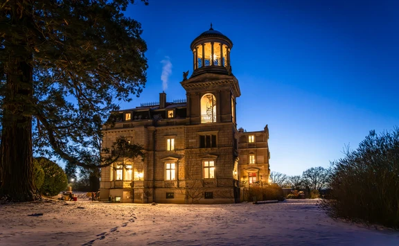 Schloss Kaarz mit Blick vom Mammutbaum zum hellbeleuchtetem Schloss in blauer Stunde mit Schnee