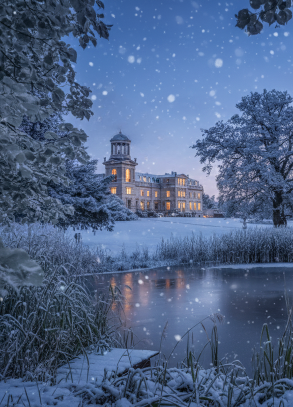 Schloss Kaarz im Winter mit Schnee und Blick durchs gefrorene Schilf und über den Teich im Dämmerlicht
