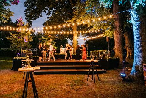 Magische Abendstimmung beim Fest im Schlosspark von Schloss Kaarz Stimmungsvolle Abendveranstaltung mit Gästen und dekorativen Feuersäulen im beleuchteten Schlosspark von Schloss Kaarz.